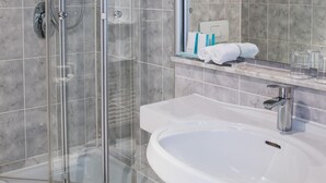 Ein modernes Badezimmer mit einer gläsernen Duschkabine, einem weißen Waschbecken und einem Spiegel.