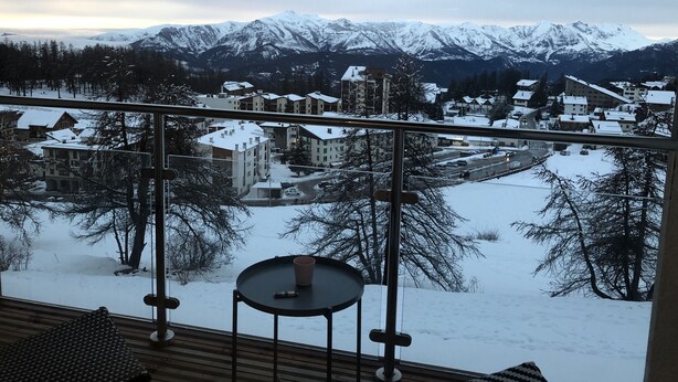 Uma varanda com vista para uma cidade coberta de neve e montanhas.