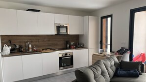 Uma cozinha moderna com armários brancos, forno embutido e painel de madeira.