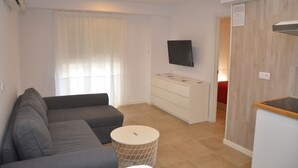 A modern living room with a grey sofa, a small round table, a TV on the wall, and a wooden cabinet. - City Suites Apartments (Valencia)