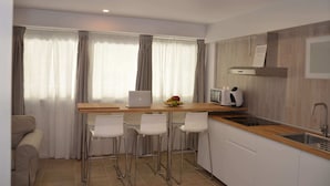 A modern kitchen with a wooden countertop, white bar stools, a laptop, a microwave, and a fruit bowl. - City Suites Apartments (Valencia)