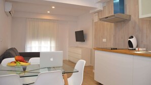 A modern kitchen with a built-in stove, a microwave, and a coffee maker. There is a dining table with chairs and a laptop. - City Suites Apartments (Valencia)