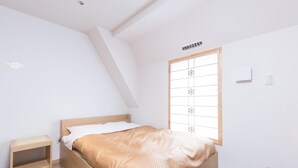 A bedroom with a bed, a nightstand, a window with a grid pattern, and a ceiling with a sloped design. - Oyo 44646 Wa Style Tokyo (Kawaguchi)