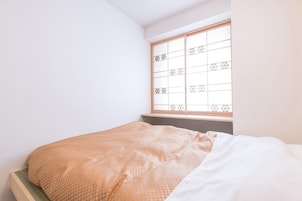 A bedroom with a bed, a window with a geometric pattern, and a plain wall.
