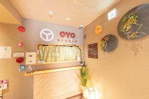 A reception area with a wooden reception desk, a clock, and a wall-mounted sign with the name 'OYO RYOKAN'.