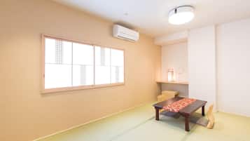 A room with tatami flooring, a low table with a red mat, a chair, and a wall-mounted air conditioner.