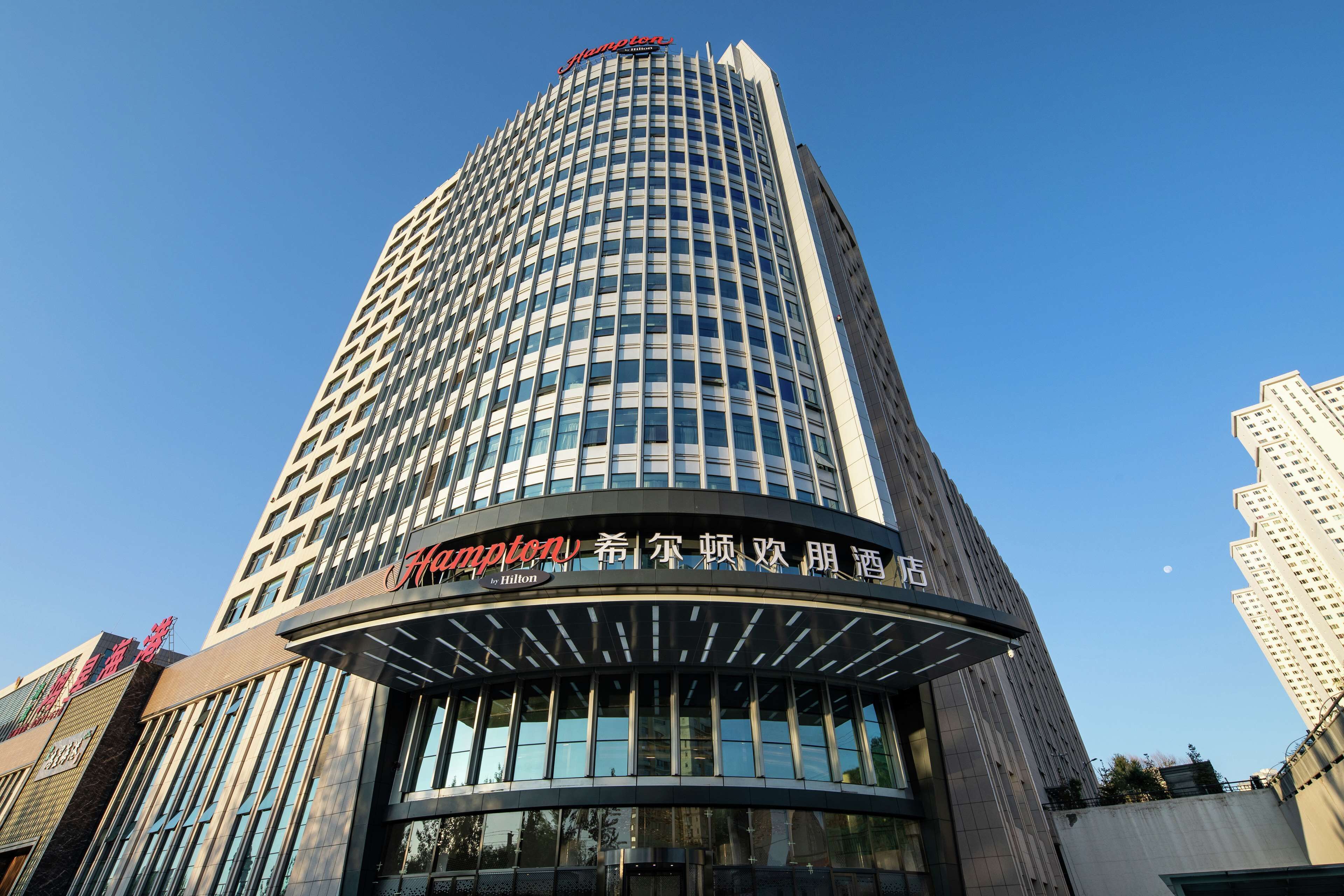 Un grand immeuble d’hôtel, sur lequel on peut voir une enseigne bien visible indiquant les noms « Hyatt » et « Hilton », ce qui montre qu’il fait partie de la chaîne hôtelière Hilton.