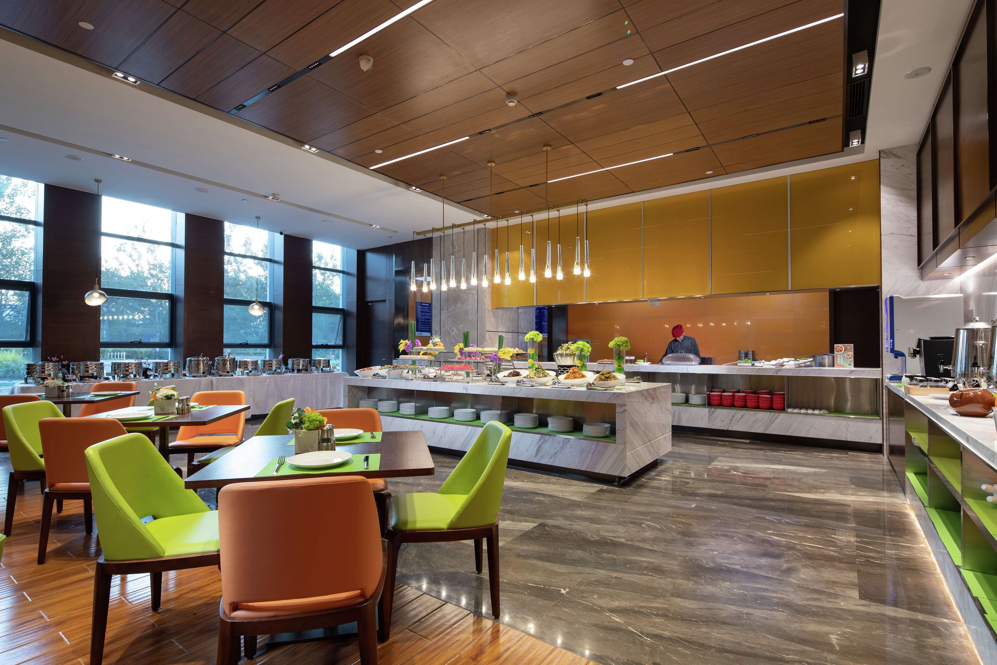 A modern restaurant with a central island, bright green and orange chairs, and a marble countertop.