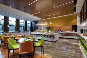Un ristorante moderno con un'isola centrale, sedie verde brillante e arancioni, e un bancone in marmo.