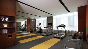 Ginásio de hotel com esteiras, elípticos e um banco de musculação.
