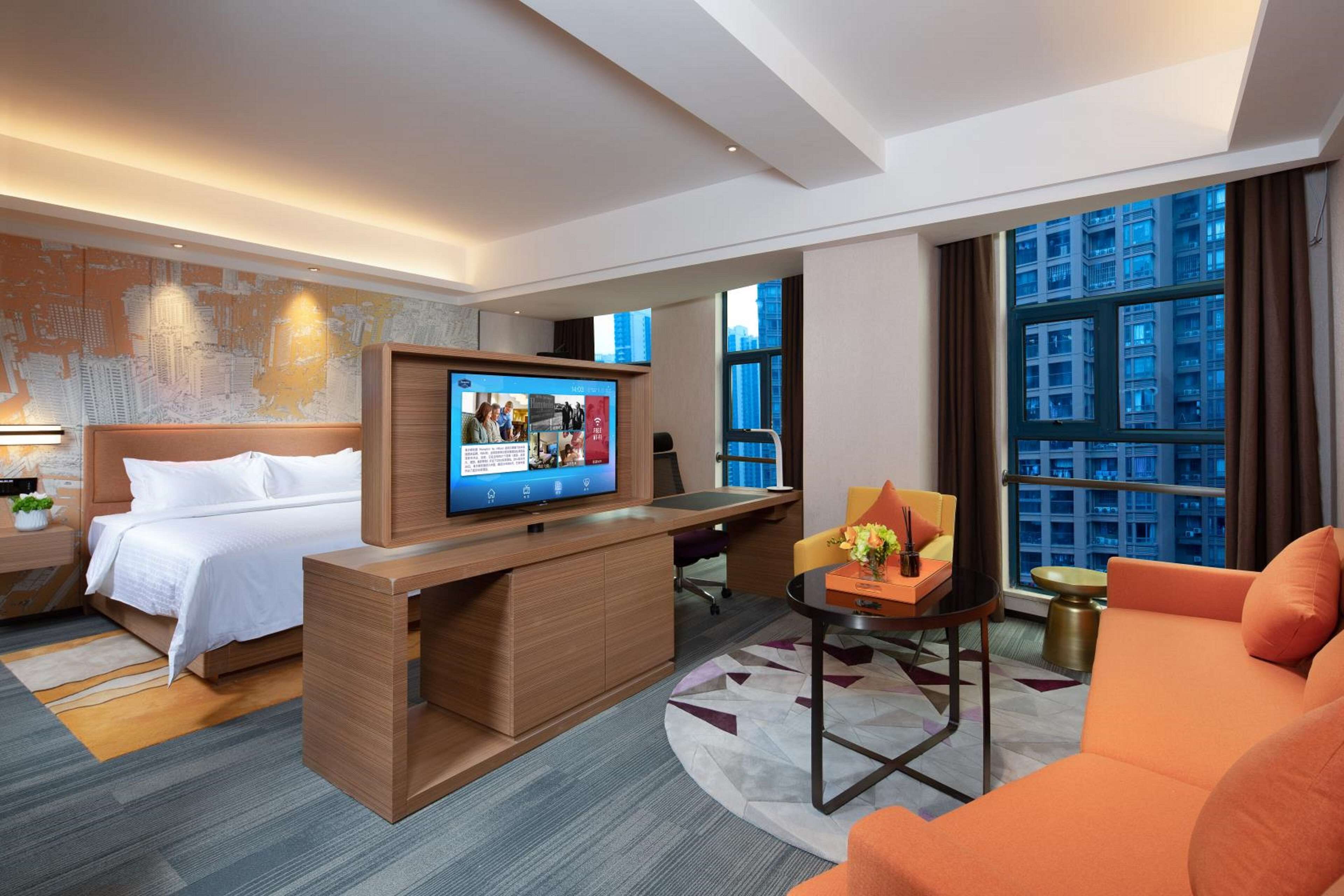 A modern hotel room with a bed, a desk, a television, and a sofa.