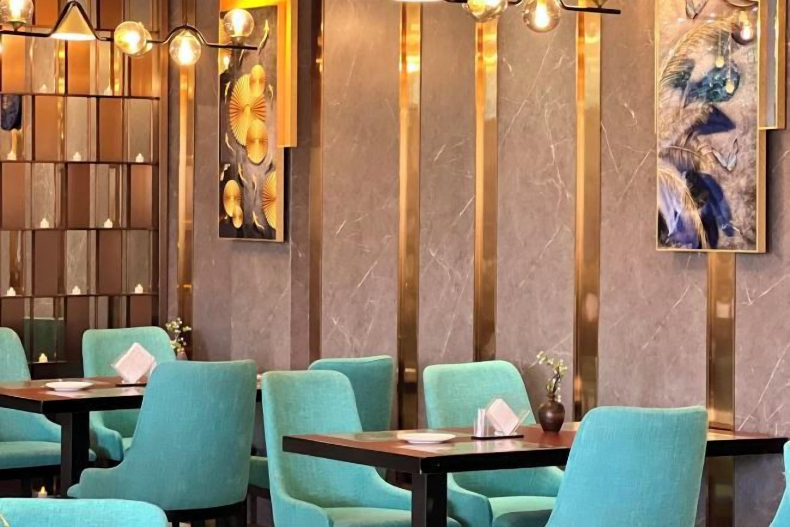 A restaurant interior with teal chairs, dark tables, and modern lighting fixtures.