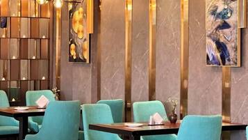 A restaurant interior with teal chairs, dark tables, and modern lighting fixtures.