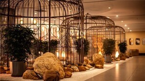 Un hall d’entrée avec un chemin central, bordé de grandes sculptures sphériques et de cages à oiseaux en métal.