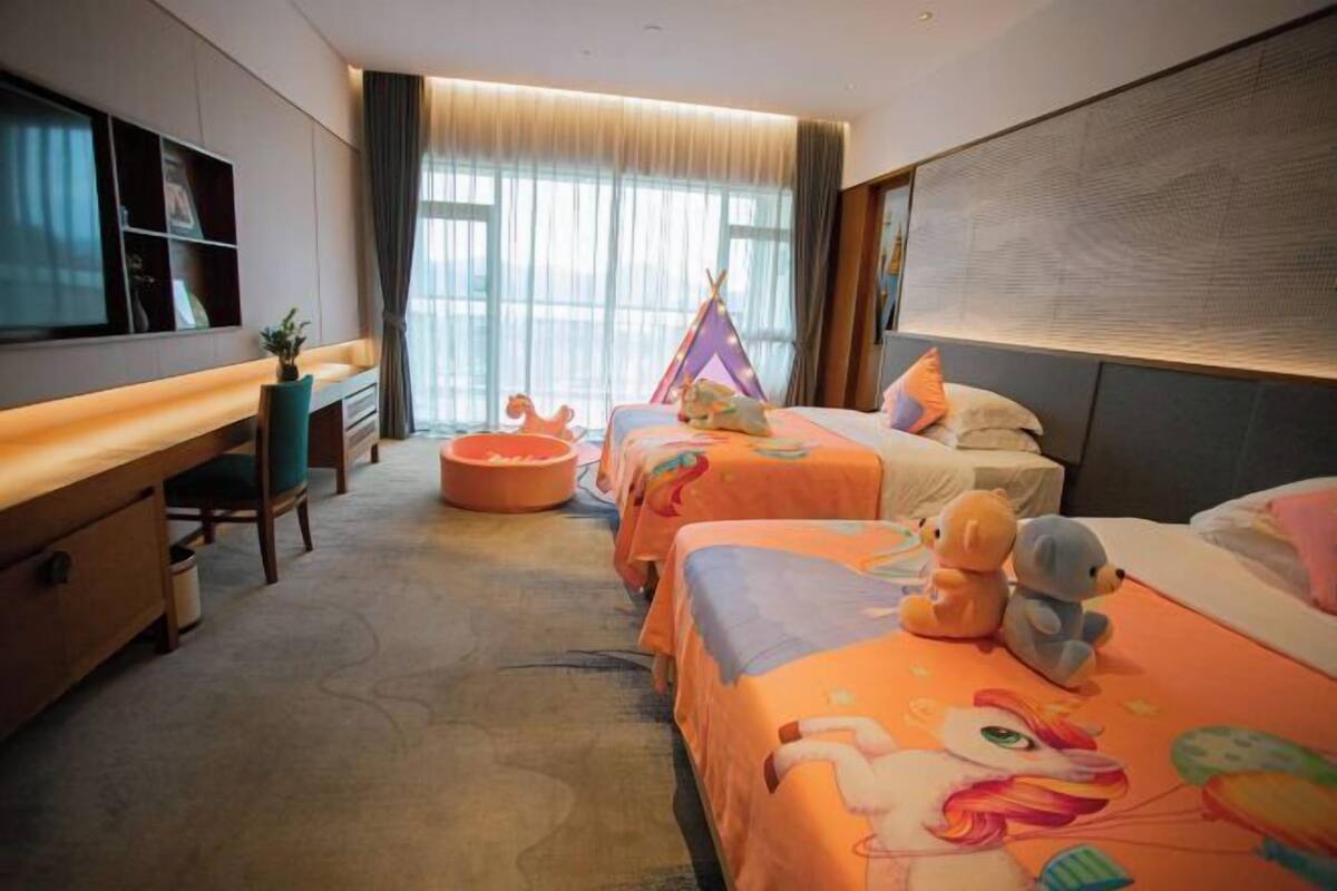 Habitación de hotel con dos camas, un escritorio, una silla y un ventanal con cortinas.