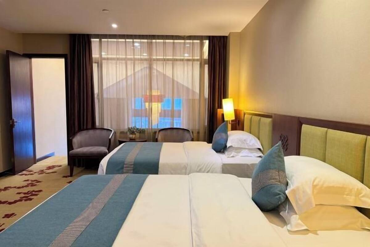 Habitación de hotel con dos camas, una silla, un escritorio y una ventana con cortinas.