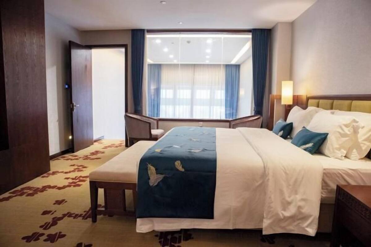 Una habitación de hotel con cama, mesita de noche y ventana con cortinas.