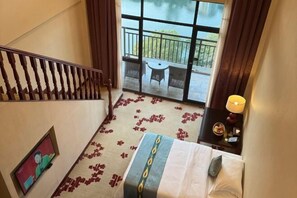Een hotelkamer met een bed, een televisie, een balkon met een tafel en stoelen, en een trap.