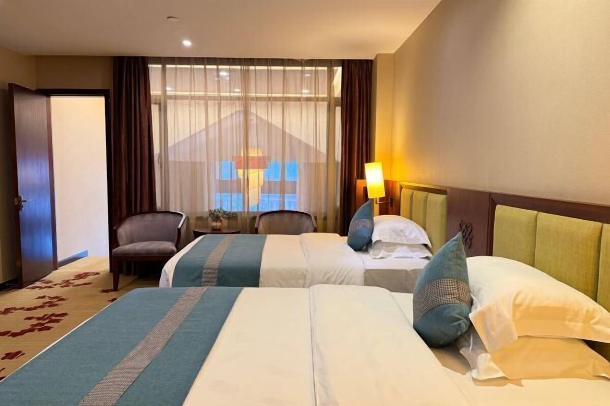 Een hotelkamer met twee bedden, een stoel, een bureau en een groot raam met gordijnen.