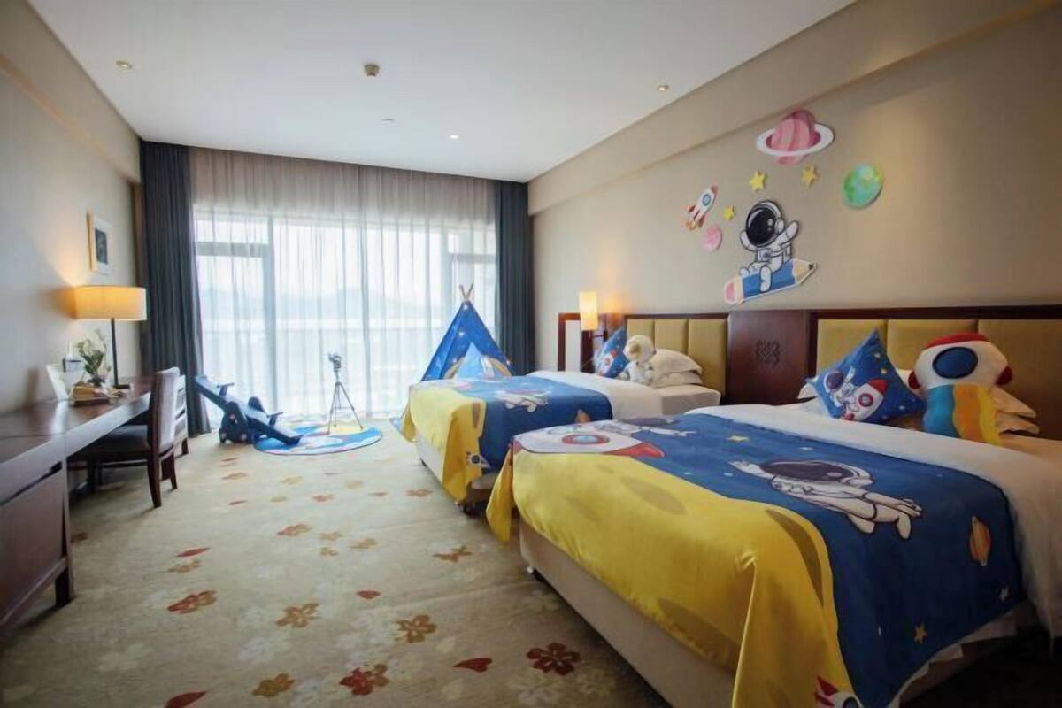 Habitación de hotel con dos camas, un escritorio, una silla, una ventana con cortinas y adornos en la pared.