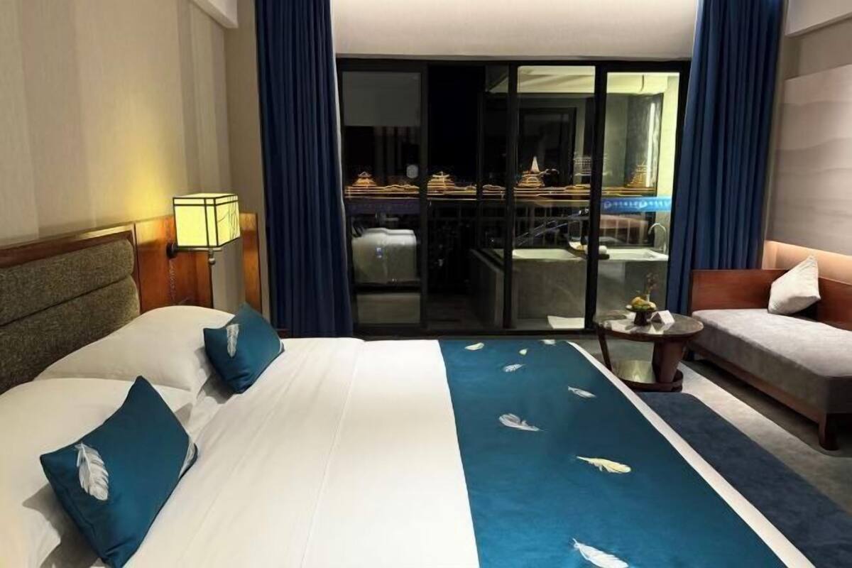 Habitación de hotel con cama, sofá, una mesita y vistas a un balcón con comedor.