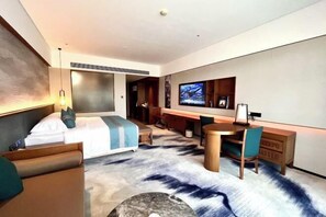Een moderne hotelkamer met een bed, bureau, stoel en een aan de muur bevestigde televisie.