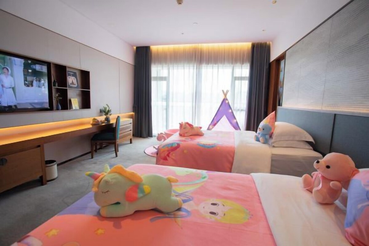 A hotel room with two beds, a desk, a TV, and a tent.