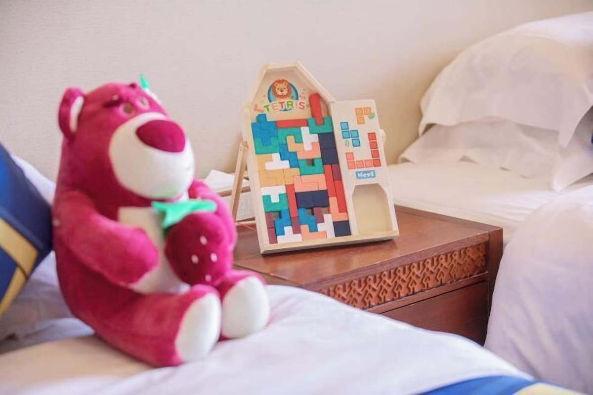 A bed with white bedding, a wooden nightstand with a puzzle game, and a pink stuffed toy.