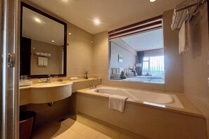 Une salle de bain moderne dotée d’une grande baignoire, d’un meuble-lavabo avec miroir et d’une fenêtre offrant une vue sur la pièce.