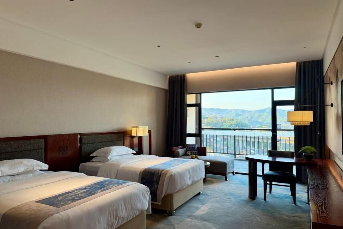 Een hotelkamer met twee bedden, een klein tafeltje en uitzicht op bergen door grote ramen.