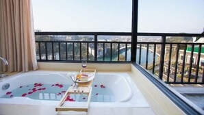 Un balcon avec une baignoire, un verre de vin, des pétales de rose et un plateau avec des livres et une bougie.