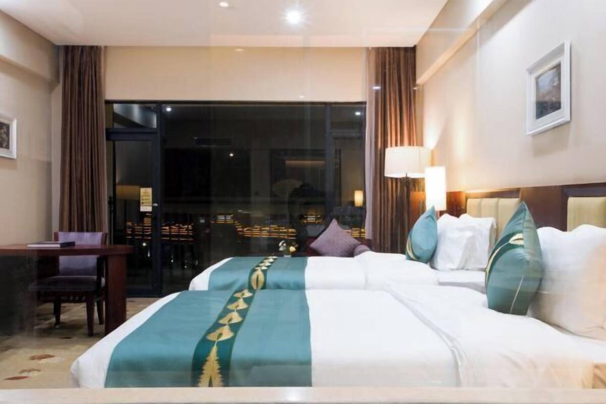 Habitación de hotel con una cama grande, un escritorio y vistas a la ciudad por la ventana.