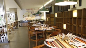 Un ristorante con tavoli rotondi, sedie di legno e lampade a sospensione verdi.