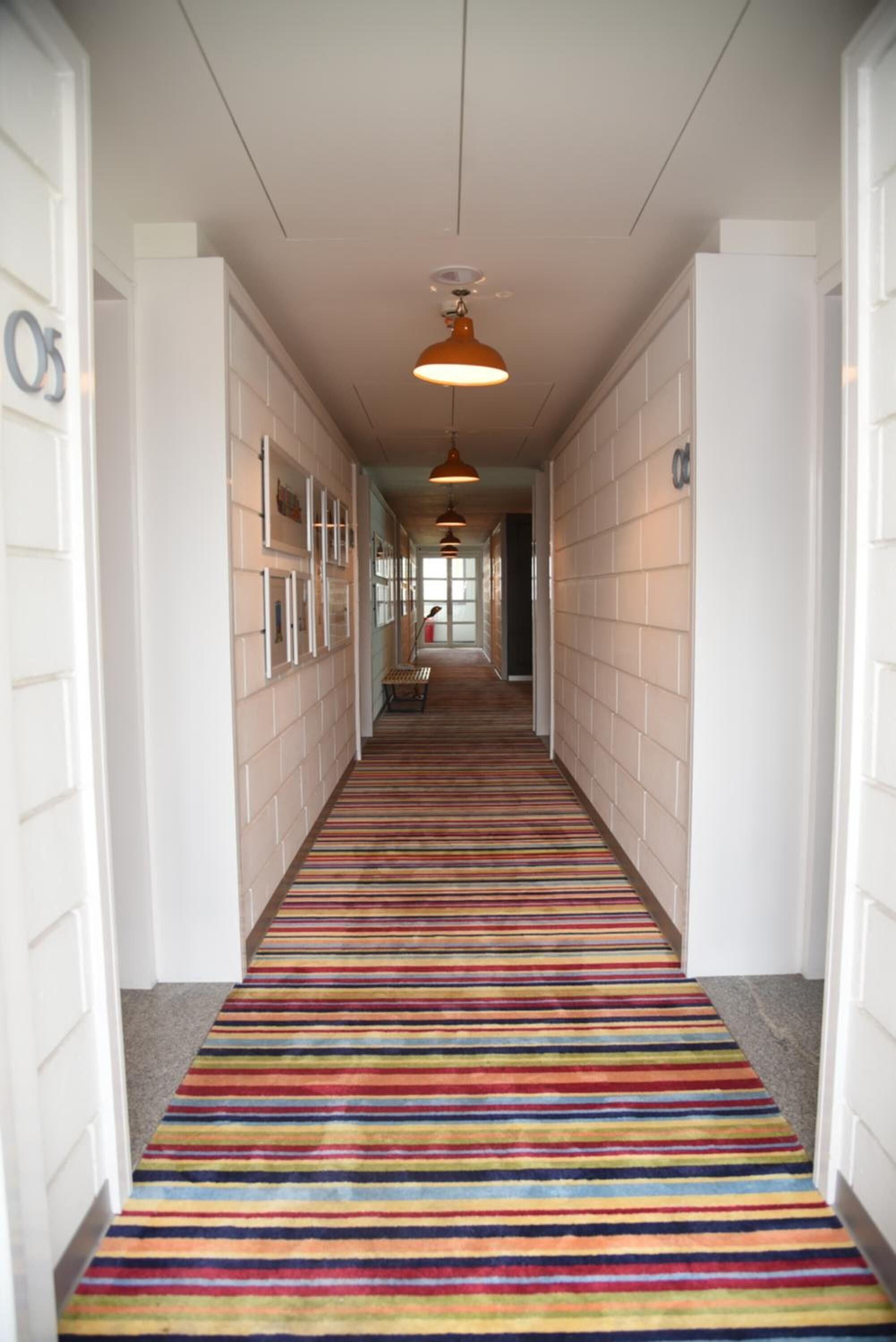 Un couloir avec un tapis à rayures, des murs blancs et des luminaires suspendus.