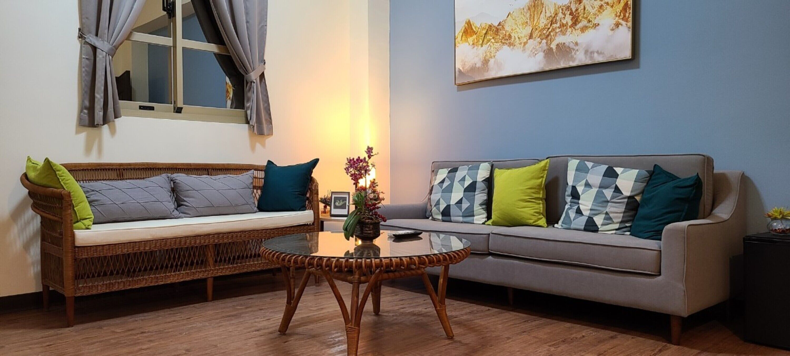 A living room with a wicker sofa, a grey sofa, and a glass coffee table.
