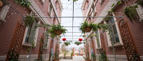 Un callejón estrecho con una estructura de pérgola de metal, plantas en macetas y faroles rojos colgantes.