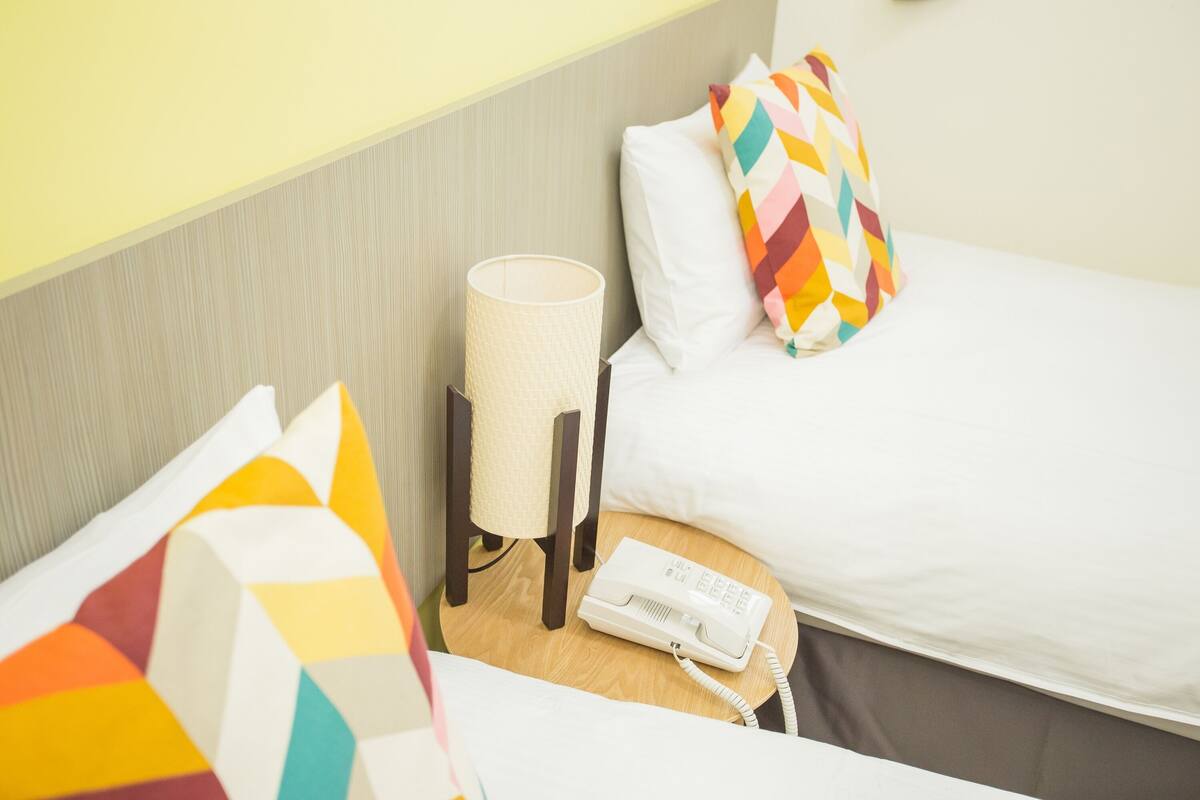 A hotel room with a bed, a bedside table with a lamp, a telephone, and colorful pillows.
