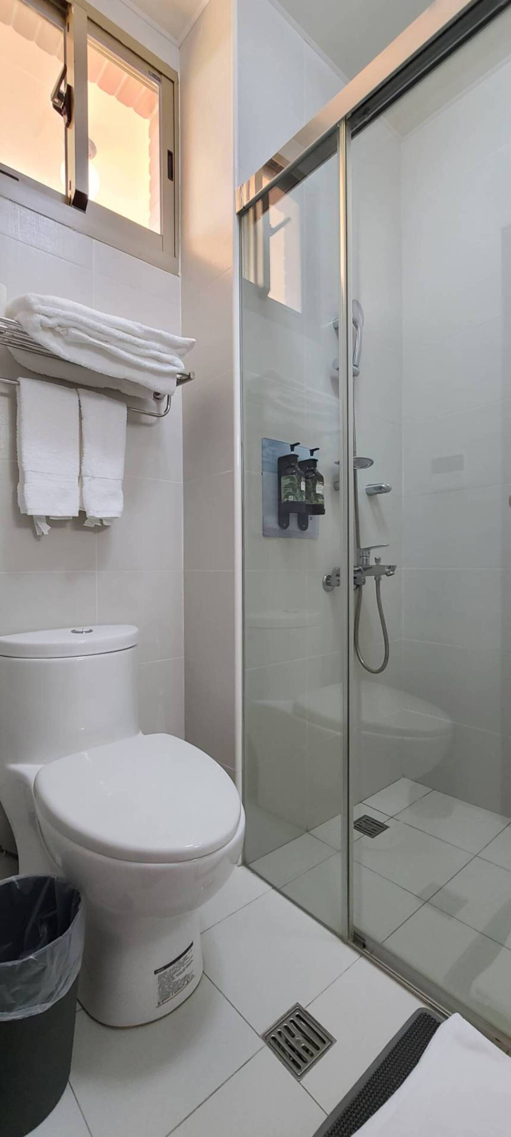 A modern bathroom with a toilet, a glass shower enclosure, and a towel rack with folded towels.
