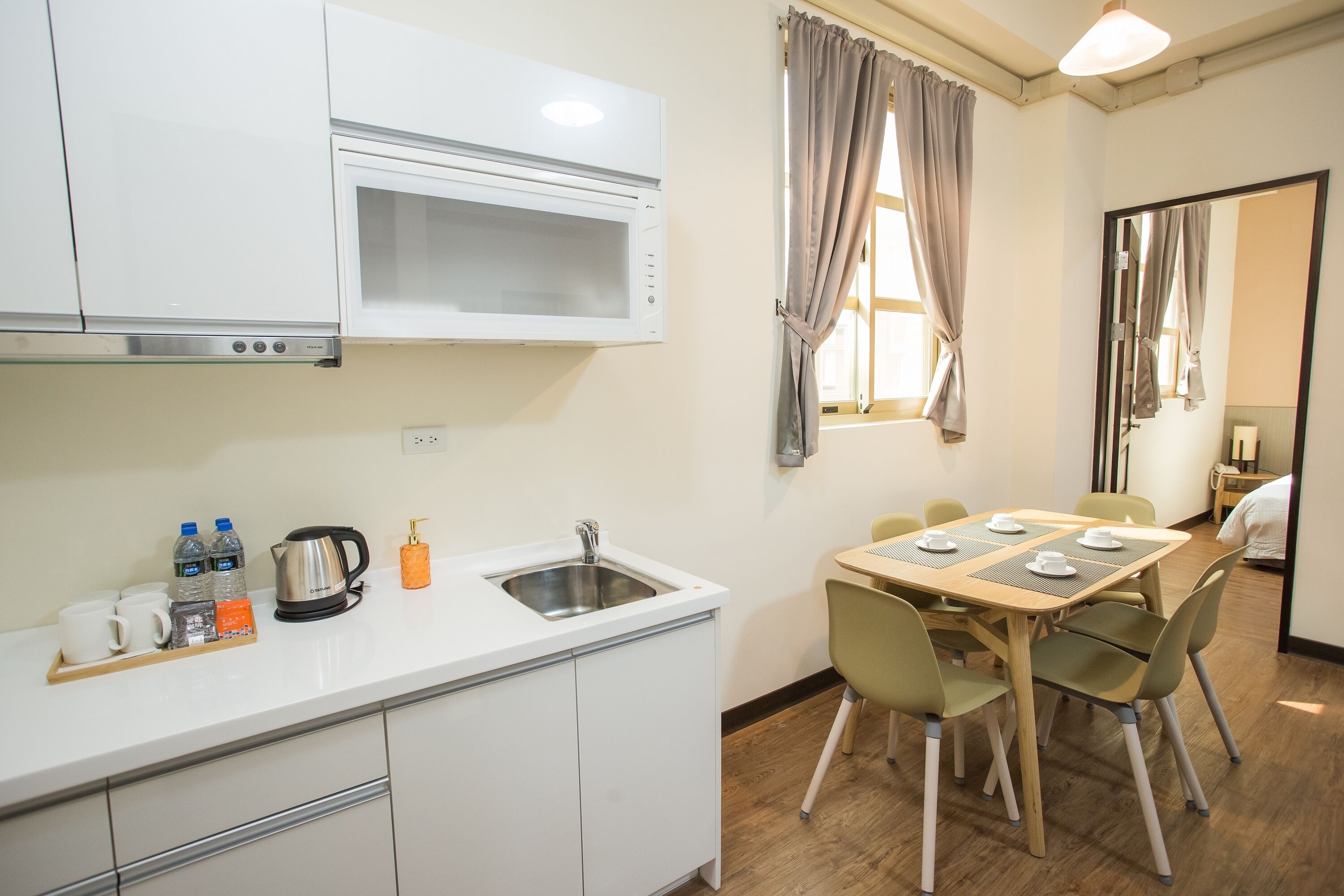 A compact kitchen with a microwave, sink, and a breakfast bar with cups and a kettle.