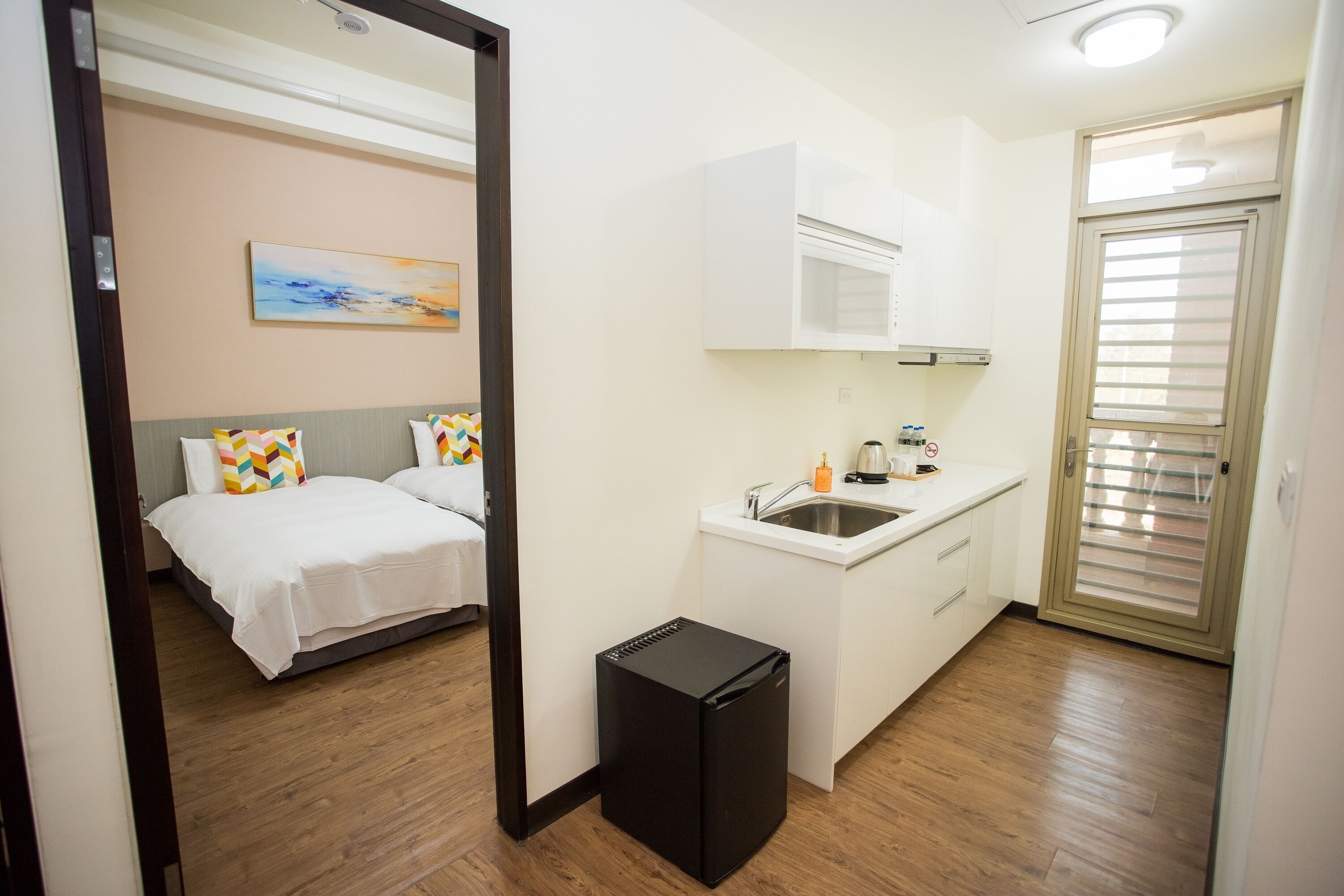 A compact hotel room with a bed, a small kitchenette, a sink, and a compact refrigerator.