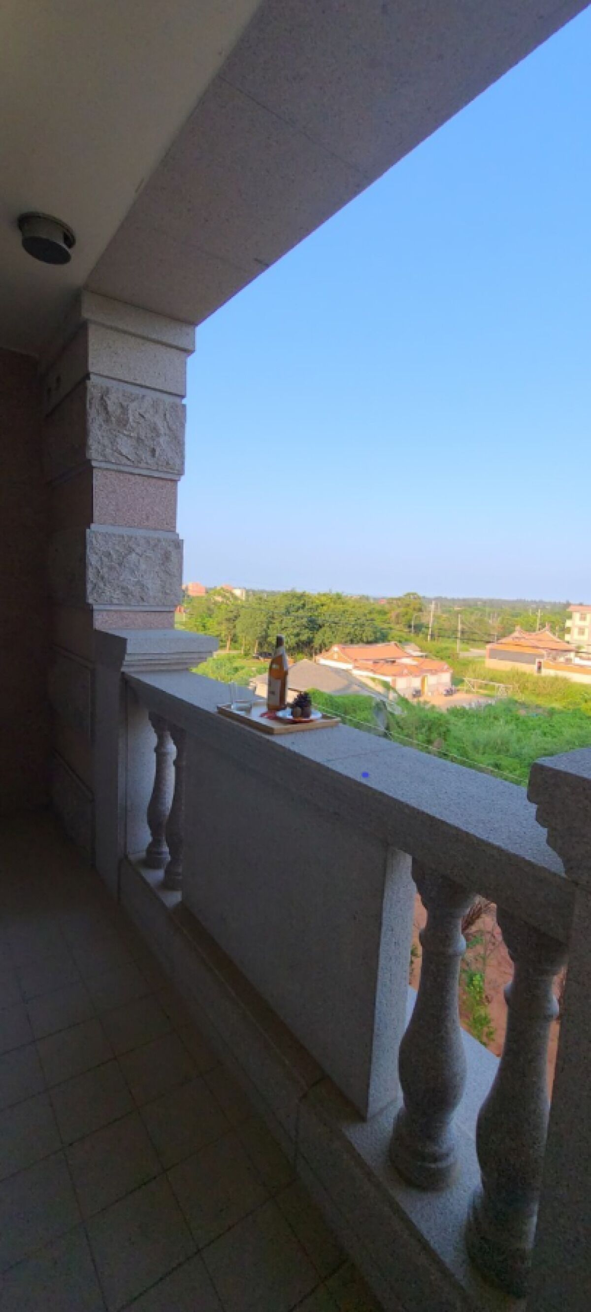 Un balcón con balaustradas de piedra y una vista despejada de un paisaje verde y edificios a lo lejos.