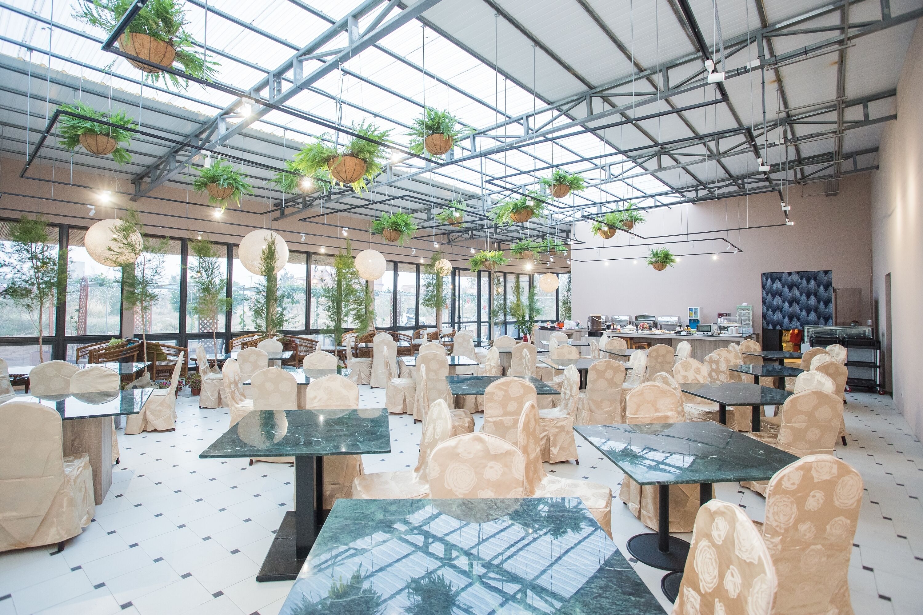 A spacious indoor area with tables and chairs, large windows, and hanging plants.