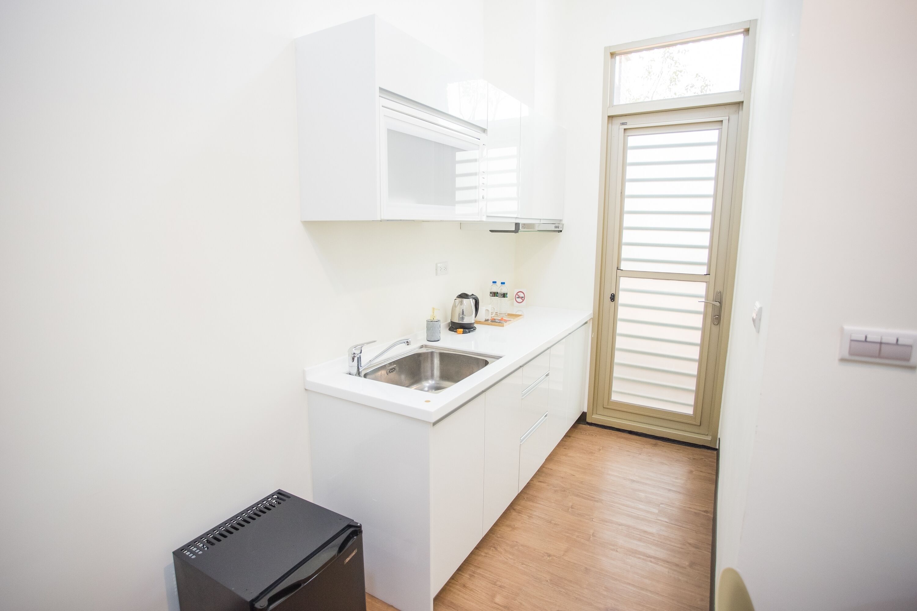 Una cocina compacta con armarios blancos, un lavamanos y un refrigerador negro.