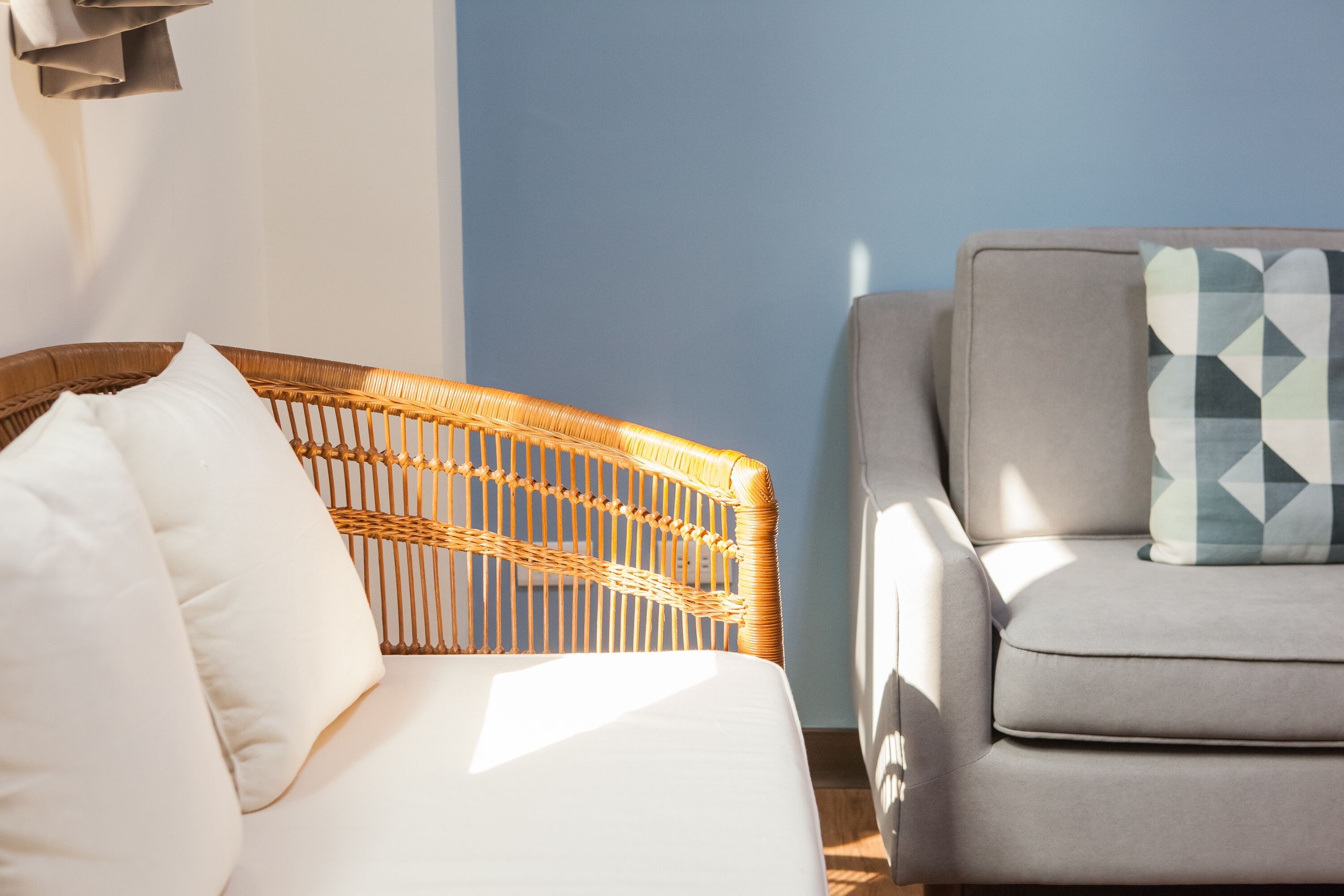 Una habitación con una silla de mimbre y un sofá gris, ambos con cojines.