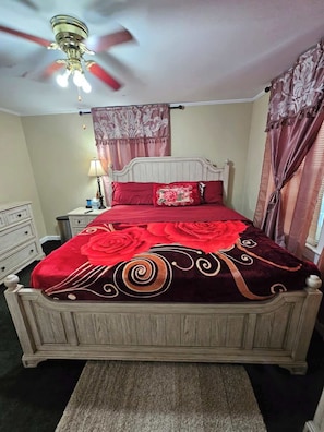 A bedroom with a wooden bed, a ceiling fan, a nightstand with a lamp, and a dresser.