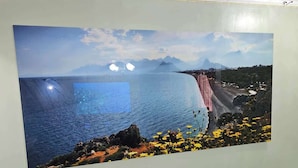 A room with a large wall mural of a coastal landscape, a black leather couch, and a vent on the floor.