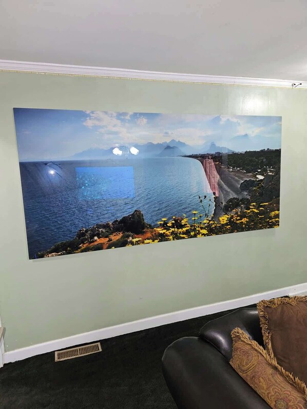 Une pièce avec une grande fresque murale représentant un paysage côtier, un canapé en cuir noir et une grille d’aération dans le sol.