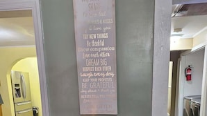 A hallway with a wall-mounted sign listing family rules, a small table with a candle, and a potted plant.
