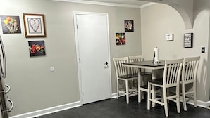 A dining area with a round table and four chairs, a white door, and a wall with framed artwork.