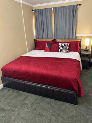 Habitació d'hotel amb un llit, una taula de nit, una làmpada i una finestra amb cortines.